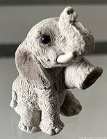 Close-up photo of a small stone elephant figurine with detailed textured surface, black eyes, and ivory tusks.