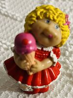 Close-up photo of Cabbage Patch Kids toy figurine with yellow curly hair, red dress and holding ice cream cone