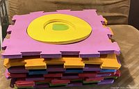 Two stacks of 10 foam alphabet puzzle mats each, showing different colored mats with alphabet letters on top layer.