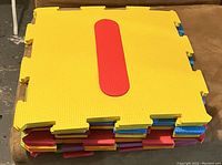 Stacked set of 10 yellow foam alphabet mats with a large red letter 'I' on the top mat. Edges show interlocking puzzle piece connectors in various colors.