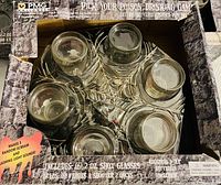 View of the six 2oz shot glasses with Halloween themed red text and images arranged in corresponding black display stand packaged in box with Halloween print.