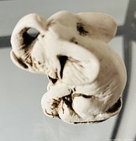 Front angled view of one white stone elephant figurine showing carved ears, trunk, and body details with darker stone markings.
