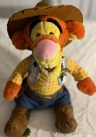Plush Tigger in sheriff outfit with cowboy hat, plaid shirt, and blue pants.