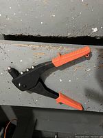 Black rivet tool featuring multiple silver rivet heads along top and orange rubber grips on handles laid on weathered wood