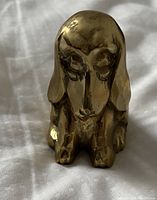 Front view of a solid brass vintage dog figurine showing facial details and sitting posture.