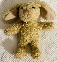 Close-up image of a vintage plush bunny showing curly beige fabric, long ears, and stitched facial details