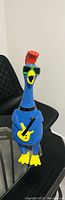 Front view of vintage Jaru rubber chicken squeak toy wearing green sunglasses and holding yellow guitar, placed on black chair and glass table.