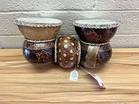 Image shows two traditional African-style talking drums and a decorated gourd shaker placed side by side on a wooden surface.