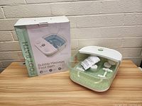 Photo showing the foot bath unit outside the box with accessories and the box displaying product info