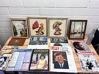 Overview of the lot with four framed pictures, vintage Kennedy magazines, and paper ephemera spread on table.
