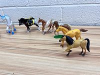 Six horse statues arranged in a row on a wooden surface, showing different colors and poses