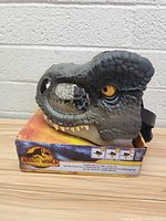 Side view of Jurassic World T-Rex mask on box showing detailed grey textured design with yellow eye and teeth.