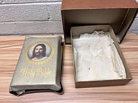 Photo of the King James Holy Bible with its decorative cover featuring Jesus image and a vintage box with white fabric inside.