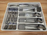 Top view of plastic tray with compartmentalized stainless steel flatware including forks, spoons, and knives.