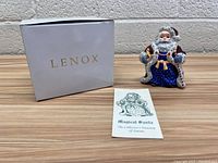 Photo showing Lenox box, Magical Santa figurine, and collector's booklet on wooden surface against cinderblock wall