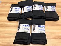 Six pairs of black Lukees fleece-lined leggings neatly stacked and displayed on a wooden surface.