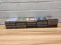 Three stacks of country music CDs in jewel cases, arranged on a white surface against a white brick wall.