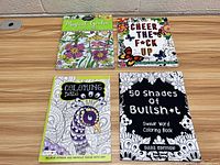 Four adult coloring books arranged on wood surface, showing front covers with colorful and black-and-white art and typography.
