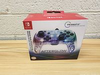 Front view of the Afterglow wired controller box showing prismatic color lighting and Nintendo Switch branding.