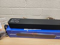 Close-up of black soundbar resting on blue Onn Blast box, showing front mesh and top control panel.