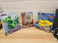 Three toys displayed together: PJ Masks Gekko Mobile in packaging, Octonauts Kwazii Adventure Pack in packaging, and Paw Patrol Rubble Bulldozer in packaging with box damage.