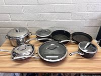 Full view of Calphalon pots and pans set on wooden table, showing six pieces including pots and frying pans with lids.