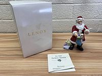 Porcelain Santa Claus figurine in red and white suit, with gifts and original white Lenox box on left, and certificate in front.