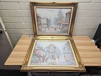 Front and angled view of two vintage gold framed impressionist style paintings on a wooden table.