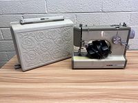 Front view of the sewing machine alongside the decorative carrying case showing embossed rose detail on case