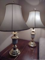 Two brass and glass table lamps with white fabric shades placed on a wooden surface, showing their overall look and height.