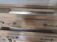 Close-up inside view of one drawer showing solid wood interior and metal handle attached to the drawer front with decorative backplates.