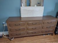 Wide front view of solid wood dresser with 9 drawers and decorative handles in a medium wood finish.