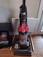 Full view of upright Dyson vacuum on wooden floor showing body, hose and cord