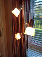 Close-up view of three white frosted glass or plastic light covers attached to a metal floor lamp, showing adjustable lamp heads turned on.