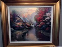 Framed Thomas Kinkade print showing a cottage by the river with colorful foliage.