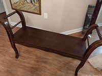 Full view of the wooden hall bench showing the seat, curved armrests, and backrest with slats on a hardwood floor.