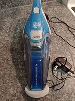 Top view of the blue and white Dirt Devil Quick Flip cordless handheld vacuum with visible filter cover and charging base beneath it.