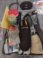 Photo showing the top of a box with various hand tools and supplies including a claw hammer, Fiskars tool in black pouch, scissors, tape rolls, and other small items.
