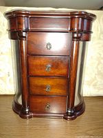 Front view of the wooden jewelry box showing four drawers with decorative metal handles and glass side panels.