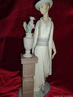 Front view of the porcelain figurine showing lady in flowing dress with decorative pillar and flower urn.