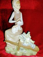 Full view of the Lladro porcelain figurine showing the girl holding a lamb sitting with a wheelbarrow of flowers nearby against a red background.