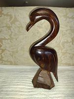 Front view of a hand carved hardwood sculpture of a long necked bird on a light patterned fabric background.