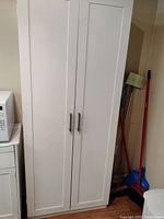 Closed view of white pantry cupboard with two doors and metal handles