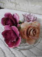 Top-down view of the four porcelain flowers in a glass dish on fabric textile background.