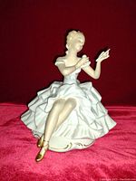 Front view of the porcelain figurine showing the sitting lady applying makeup with detailed dress and golden shoes.
