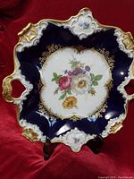 Front view of the porcelain plate showing the floral design, gold trim, and cobalt blue background with display stand.