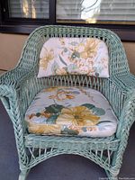 Front view of light green rattan rocking chair with floral seat and back cushions.