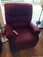 Front view of burgundy recliner with remote control resting on left arm.