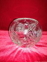 Round clear crystal bowl with starburst and fan cut designs displayed against a red background.