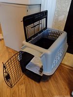 Two door kennel carrier showing front metal door open revealing absorbent pad inside.
